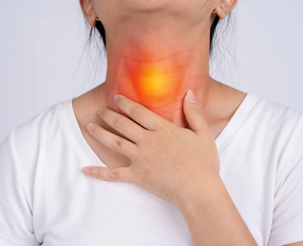 A person in a white shirt holds their neck with both hands, with a bright orange glow highlighting the thyroid area, indicating inflammation or pain, against a plain light gray background.