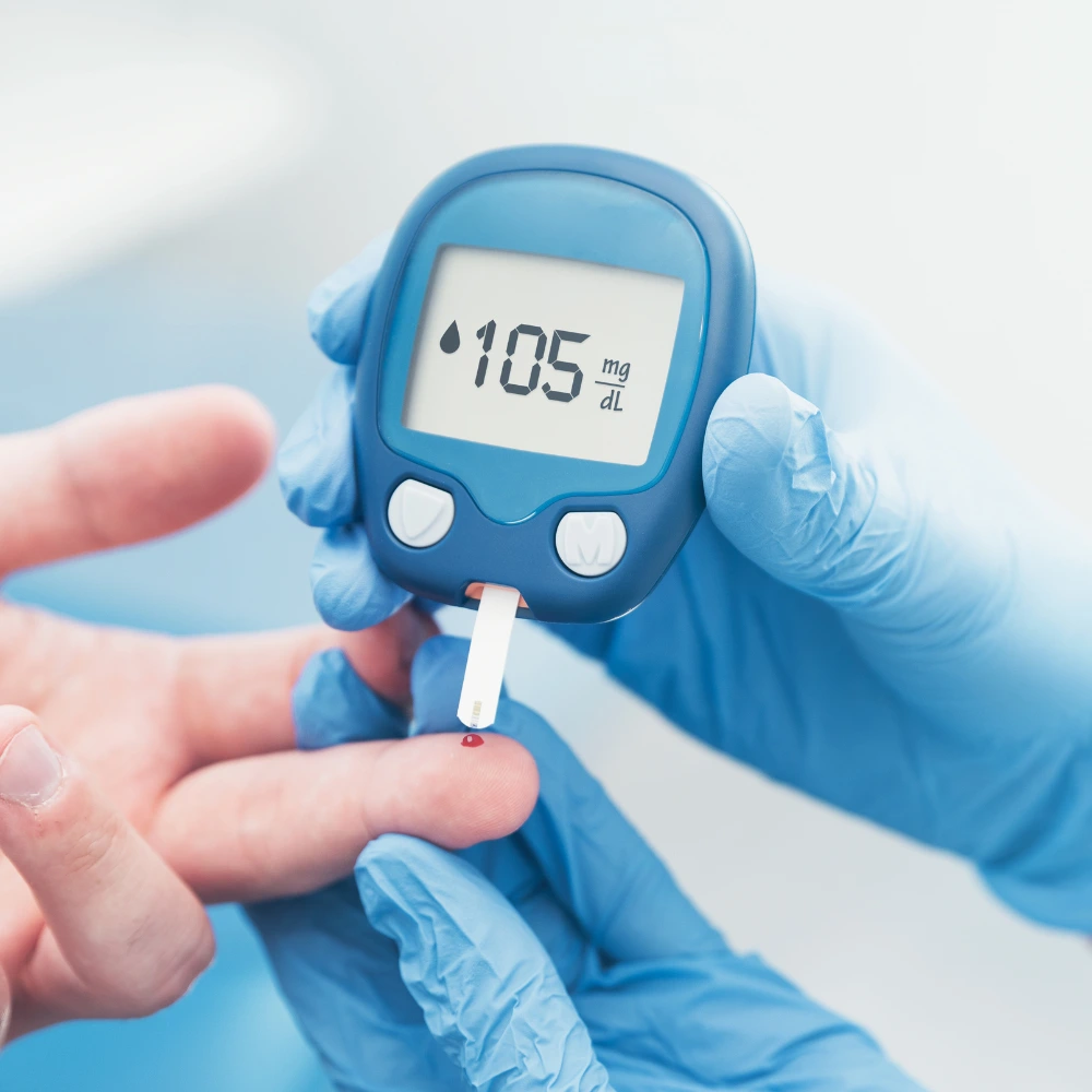 A close-up image of a gloved hand using a glucose meter to check blood sugar levels from a finger prick.