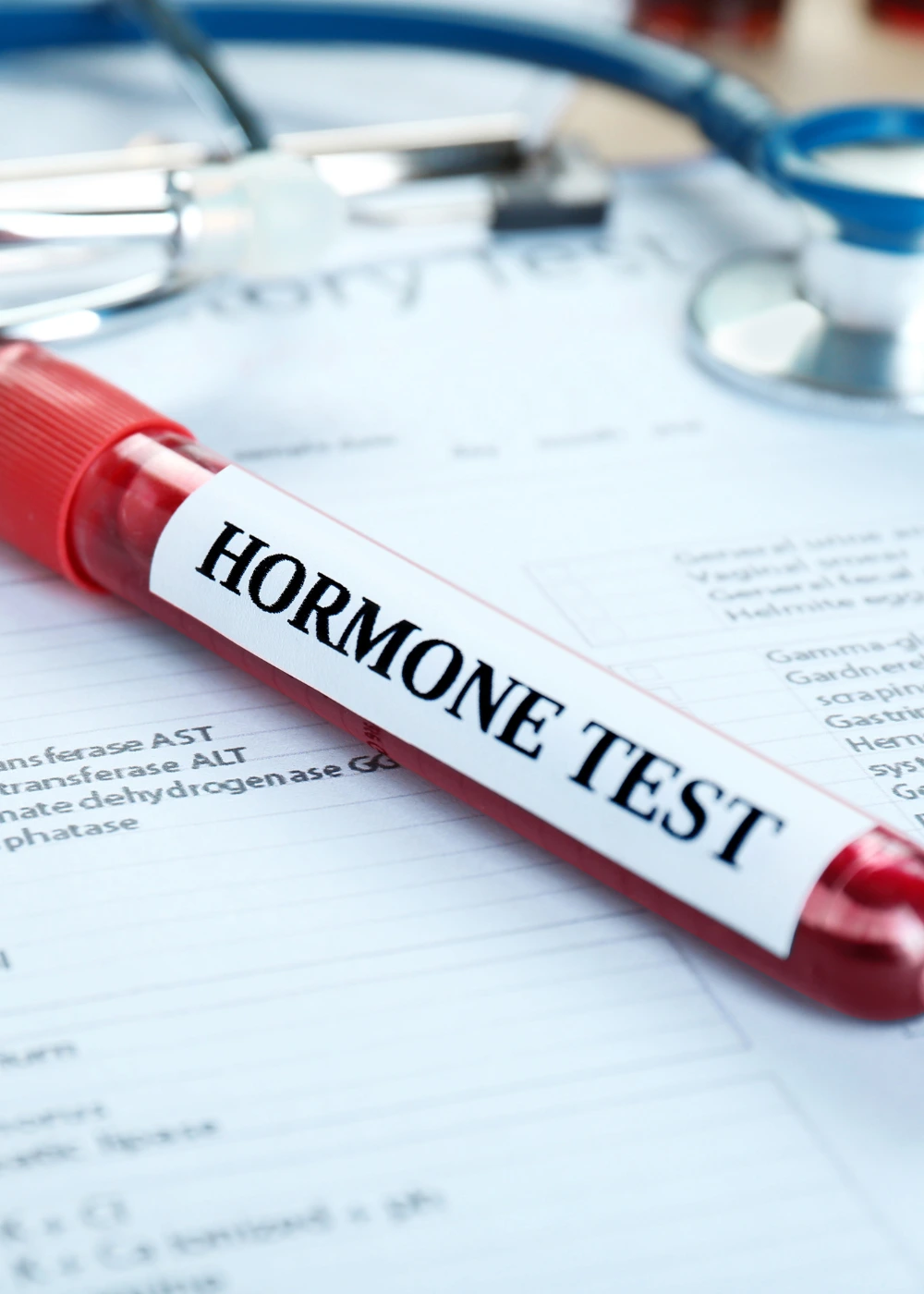 The image shows a red-capped test tube labeled "HORMONE TEST" placed on a medical form, with a stethoscope resting nearby.